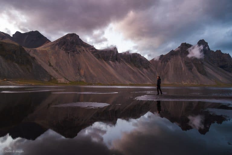 Panorama del monte Vestrahorn in Islanda in estate che si riflette sull'acqua con una piccola persona che passeggia davanti